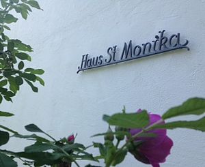 Außenwand Haus St. Monika mit gleichnamiger Aufschrift und einer Rose im Vordergrund